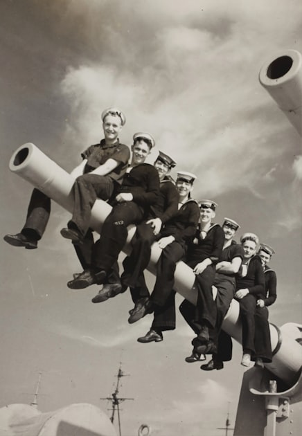 Vintage photo of navy sailors sitting on a battleship gun barrel
