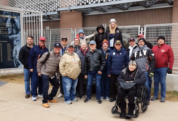 A group of people wearing winter jackets and hats posing together for a photo outside a sports stadium or arena