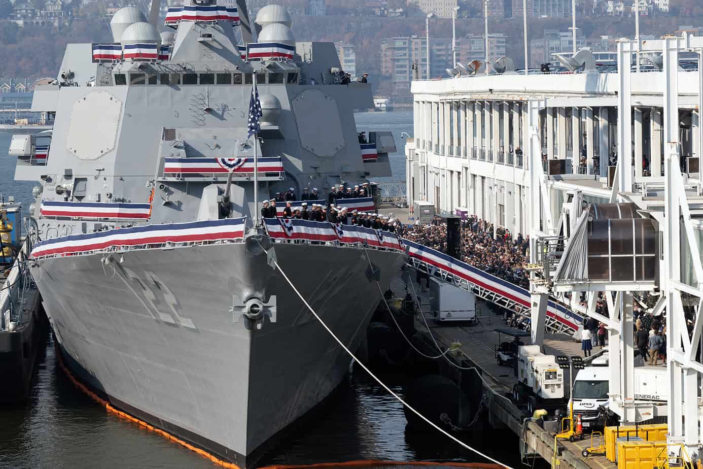 U.S. Navy Arleigh Burke-class guided-missile destroyer USS John Basilone (DDG 122) docked at a pier, decorated with patriotic bunting and lined with crew members during a commissioning ceremony