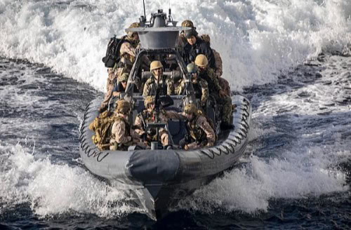 A group of U.S. Marines in an small vessel traveling towards the camera.